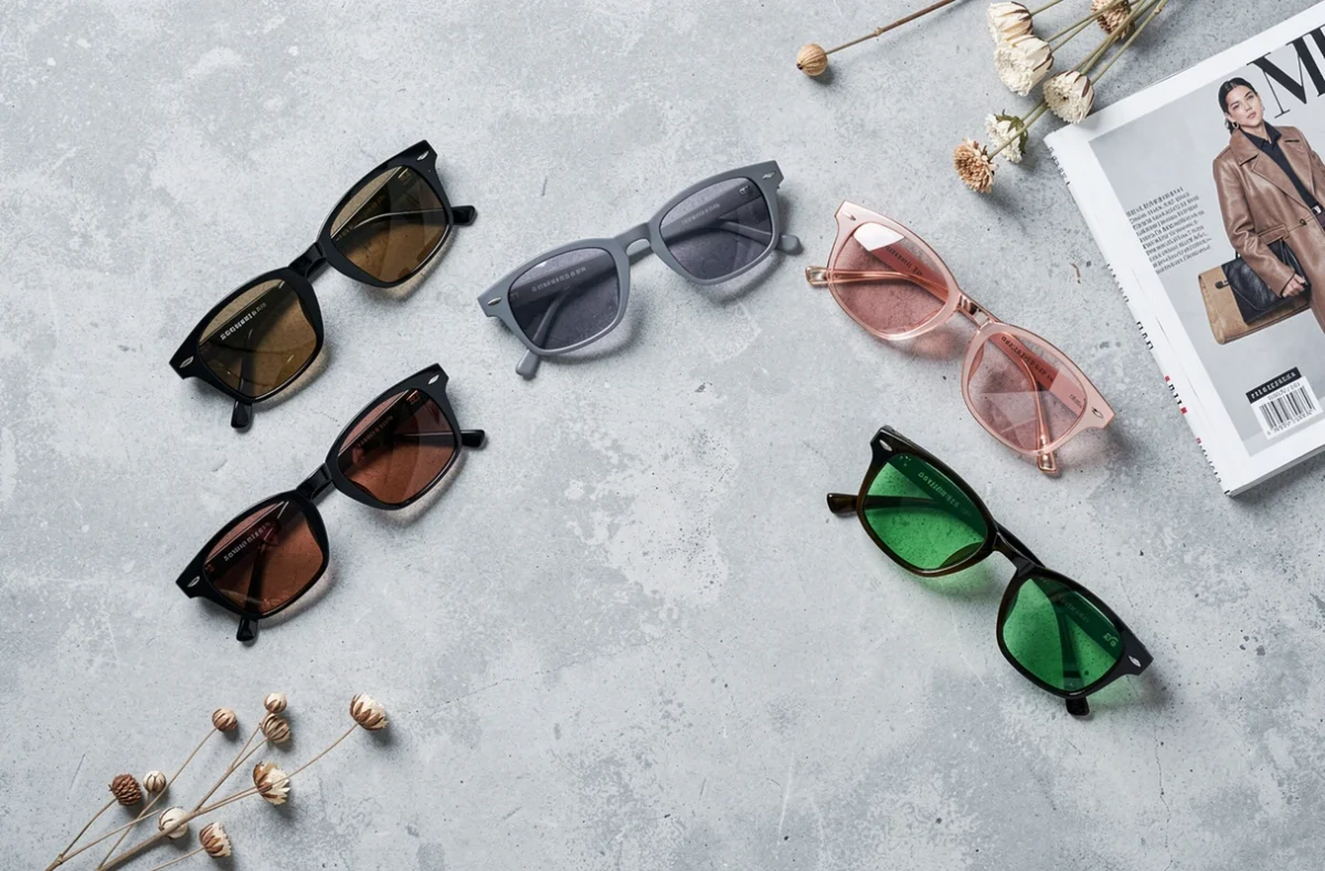 Sélection de cinq paires de lunettes de soleil aux verres de couleurs différentes disposées en flat lay sur béton gris
