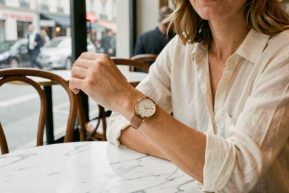 Femme au poignet fin portant une montre fine en or rose avec bracelet en cuir dans un café parisien